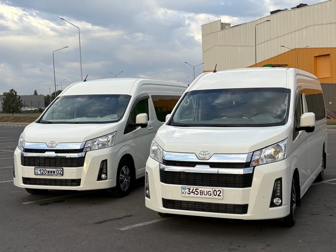 Two white high-roof Toyota Hiace minibuses parked side by side in Almaty — minibus hire with a driver