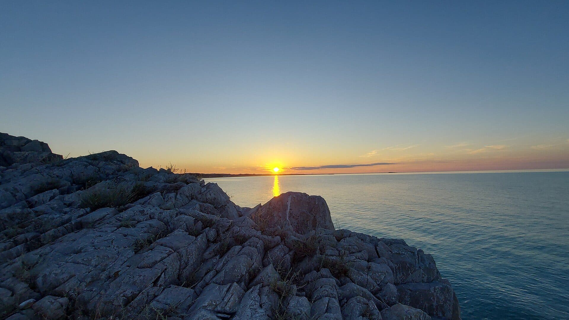 Sunset over Lake Balkhash at Mynaral: the sun sets into the water beyond the rocky shore