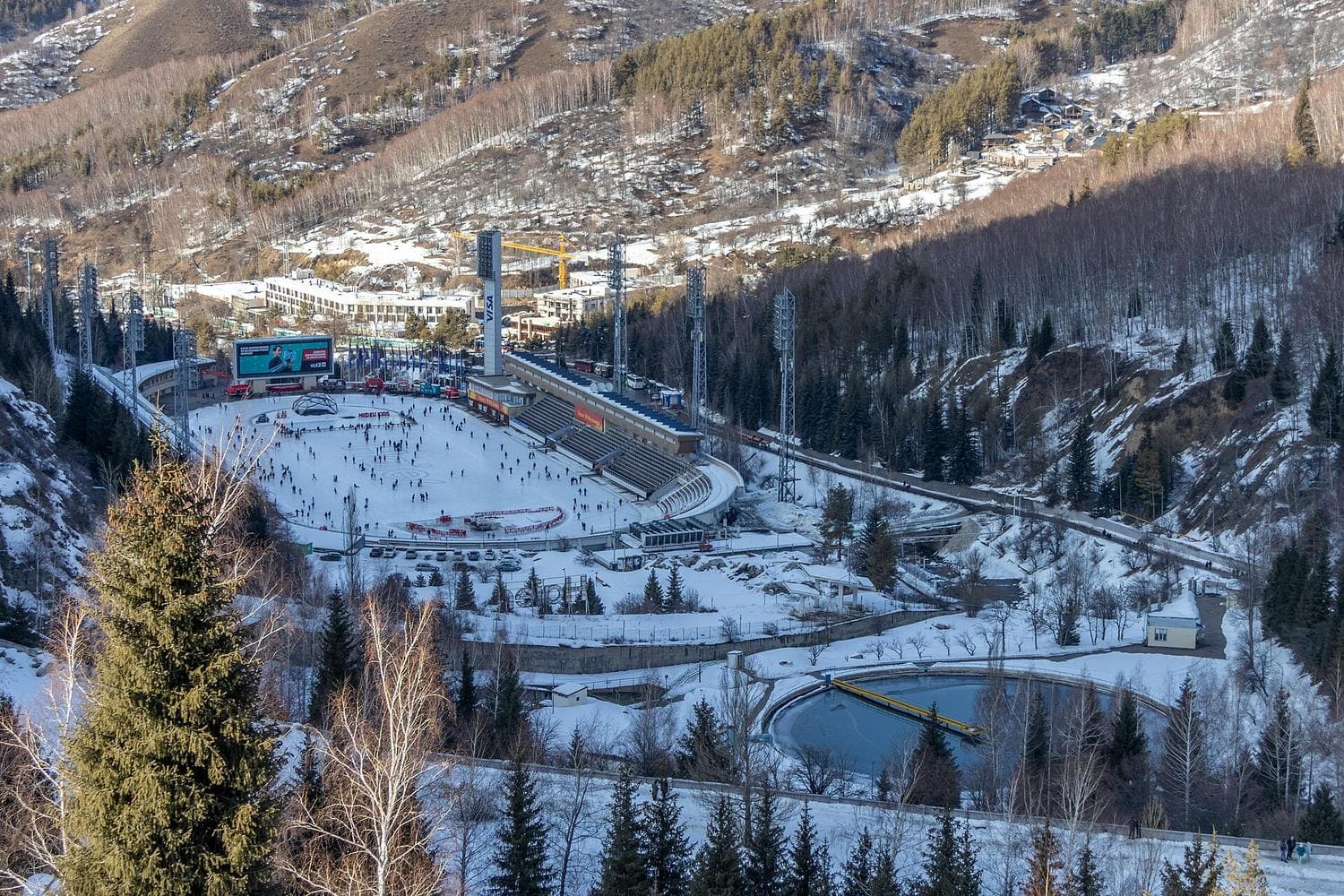Medeu skating rink from above in winter: skaters on the ice, stands and the snowy gorge (before the renovation)